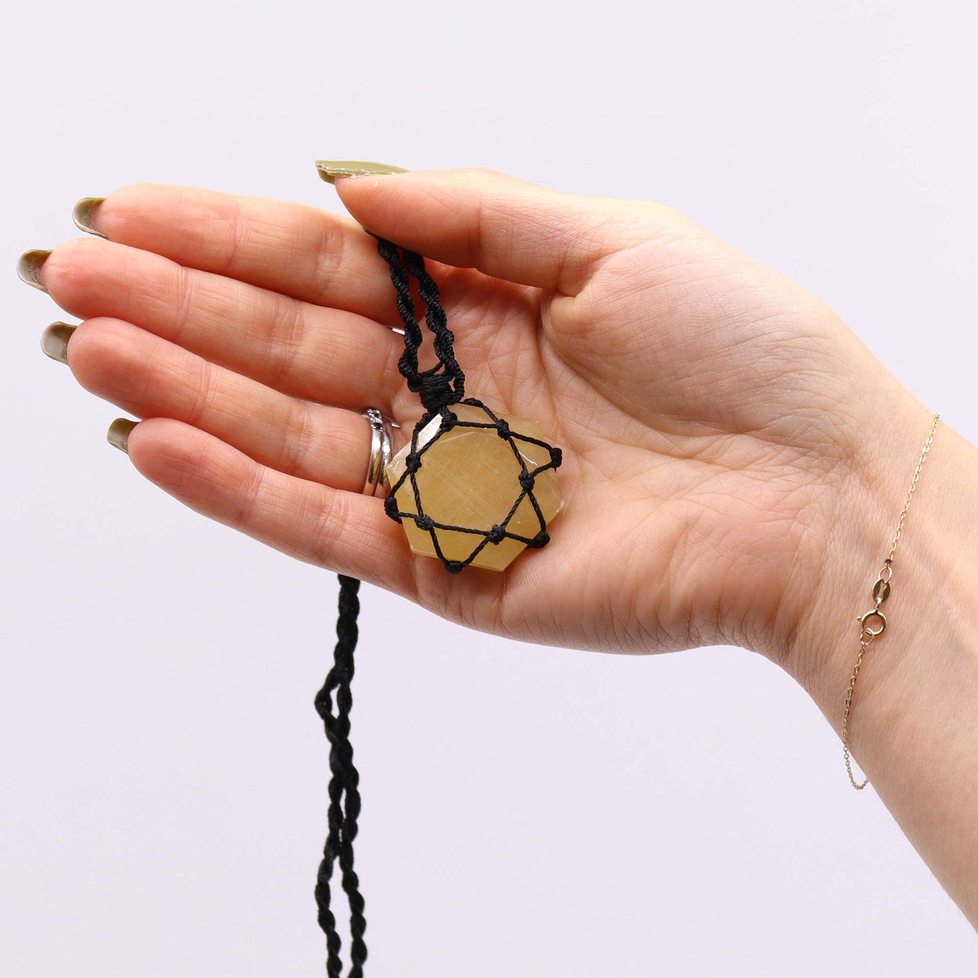 Hand holding a Laced Gemstone Hexagon Pendant - Yellow Quartz necklace against a white background