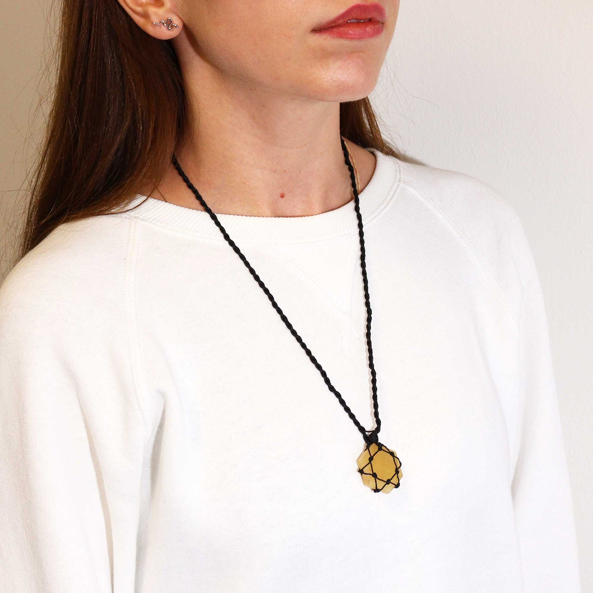 Person wearing a necklace with a Laced Gemstone Hexagon Pendant - Yellow Quartzon a plain background