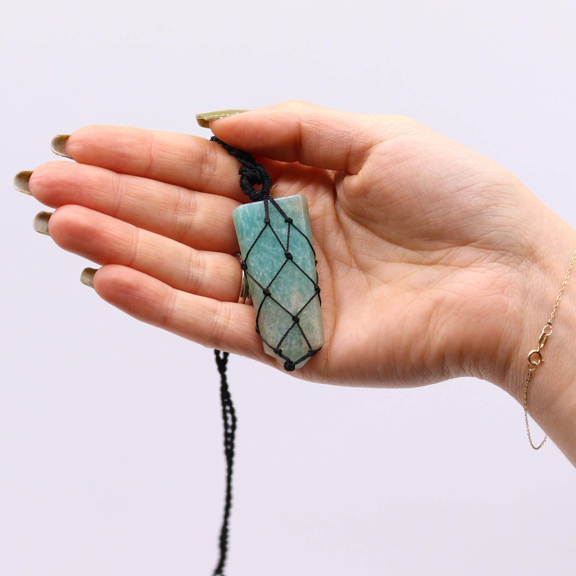 Hand holding a necklace with a green Amazonite pencil stone pendant against a light background