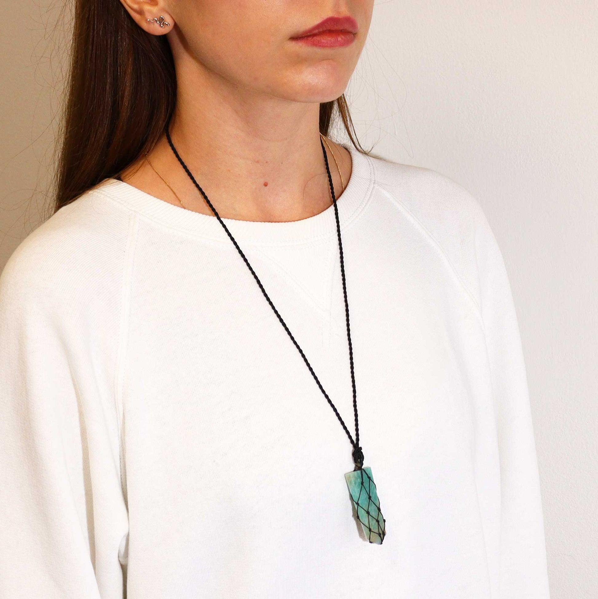 Person wearing a necklace with a green amazonite pencil pendant on a plain background