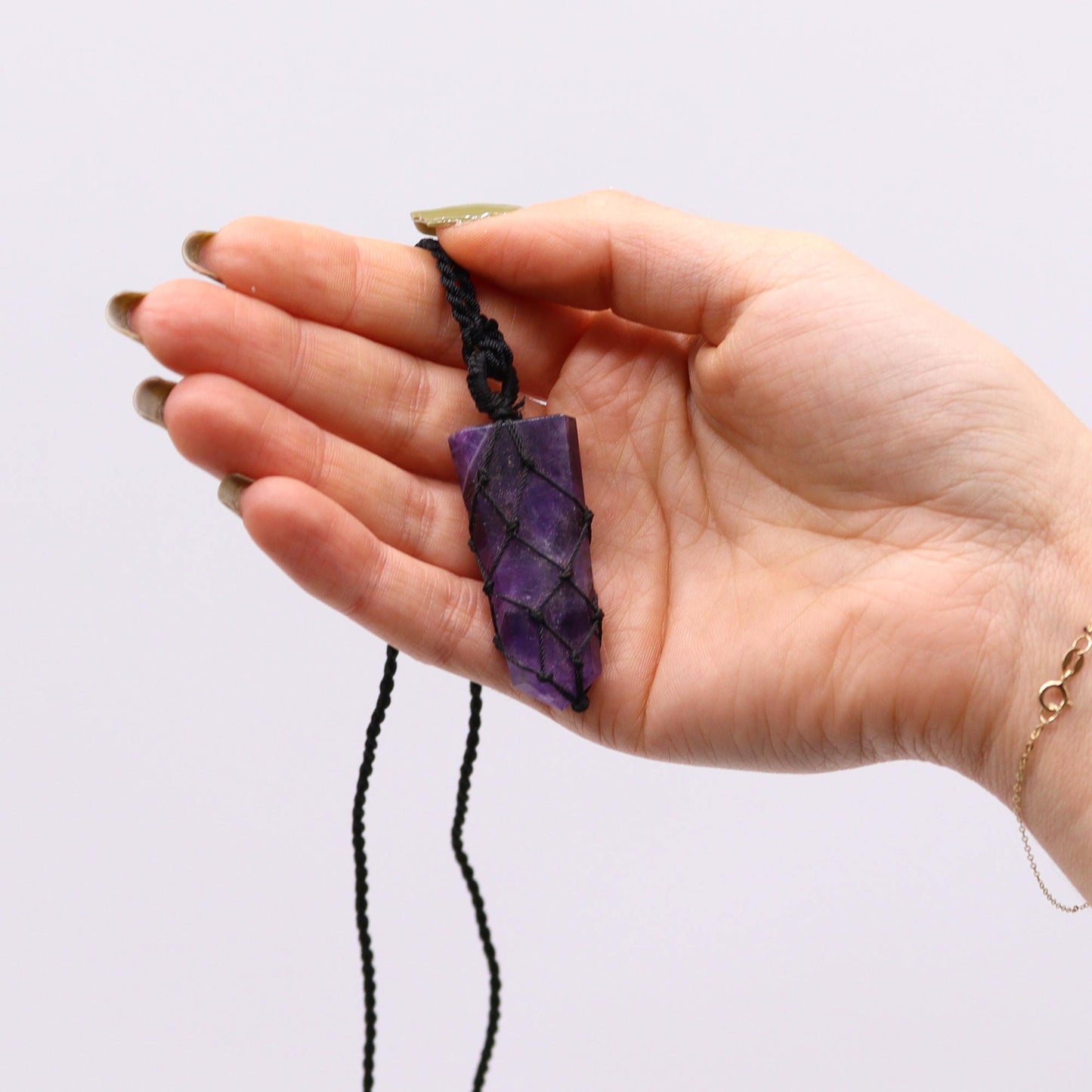 Hand holding an Amethyst crystal necklace against a white background