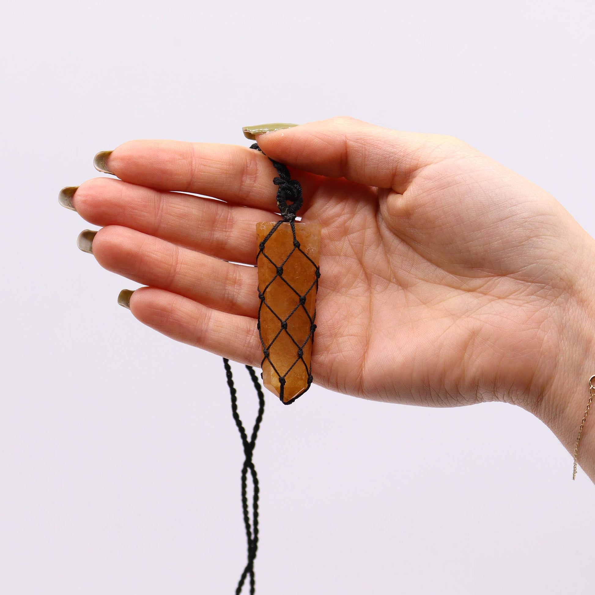 Hand holding a necklace with a Golden quartz pencil pendant against a white background