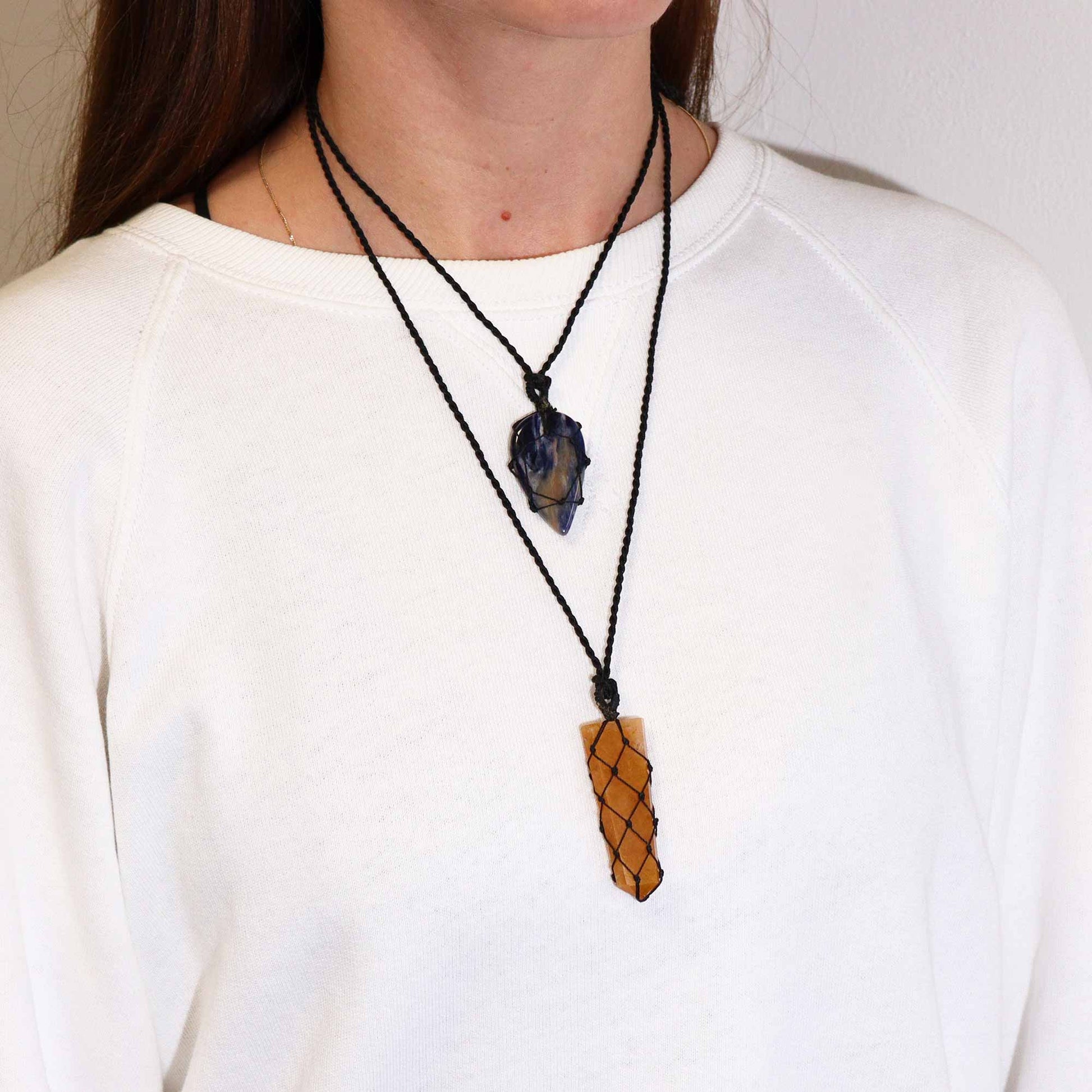 Person wearing a necklace with two pendants one is z golden quartz and the other is an amethyst on a plain background