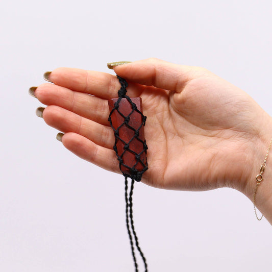 Hand holding a red Jasper stone pendant with black cord against a white background