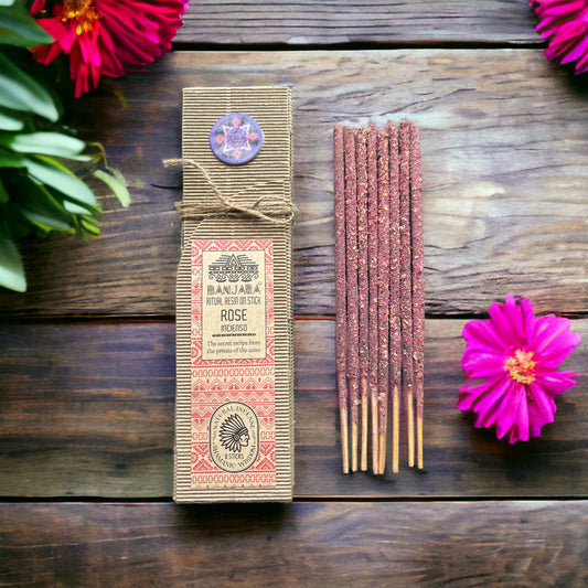 A pack of Rose incense sticks displayed on a stone surface surrounded by various small plants, with a decorative box in the background.Underground Allure Essex, UK