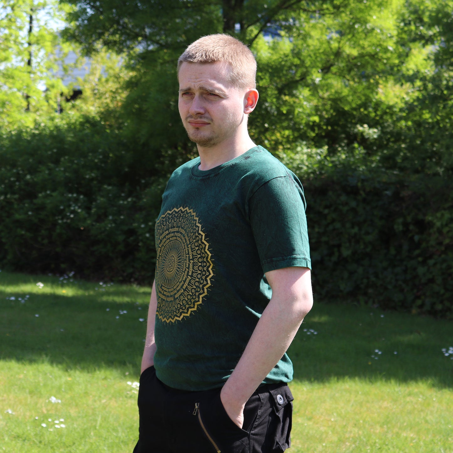 Man wearing a green t-shirt with a Mandala design in a park setting