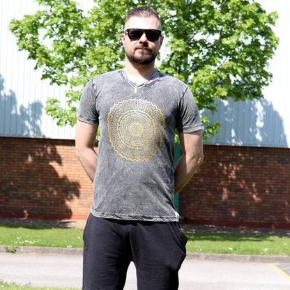 Man wearing  sun glasses & a gray t-shirt with a gold mandala design outdoors.