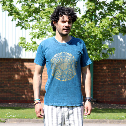 Man wearing a blue t-shirt with a gold mandala design outdoors.
