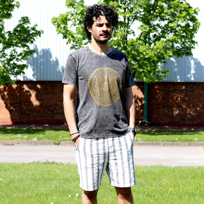 Man  with black hair wearing a gray t-shirt with a yellow design and plaid shorts standing outdoors.