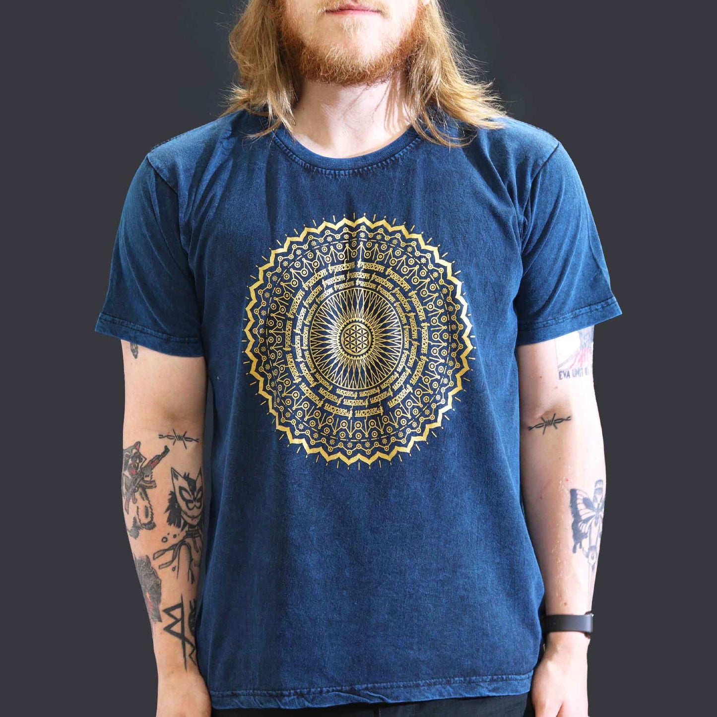 Person wearing a blue t-shirt with a gold mandala design on a plain background