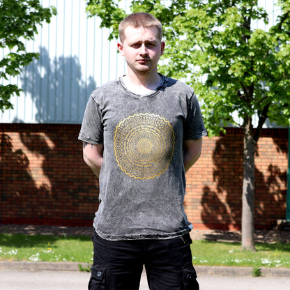 Man wearing a gray t-shirt with a gold circular design outdoors.