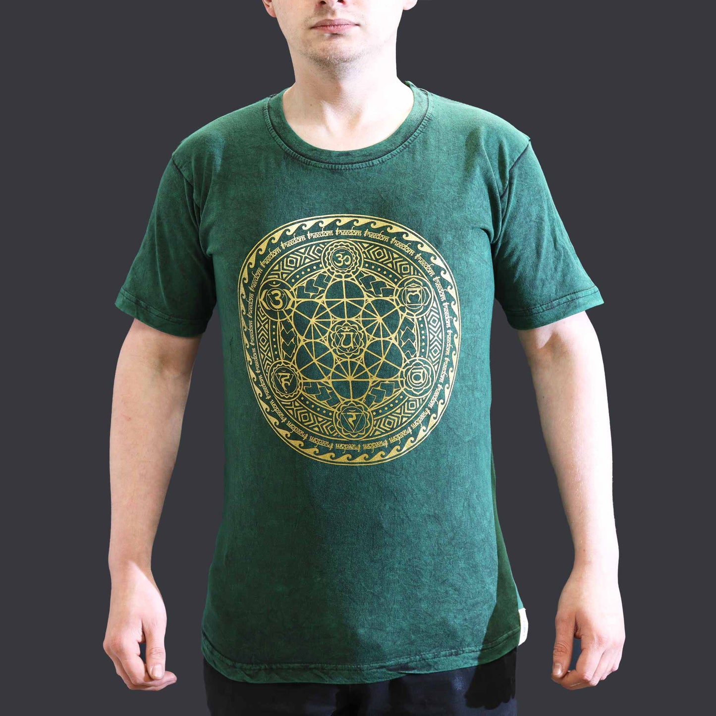 Green t-shirt with gold geometric design worn by a person on a dark background