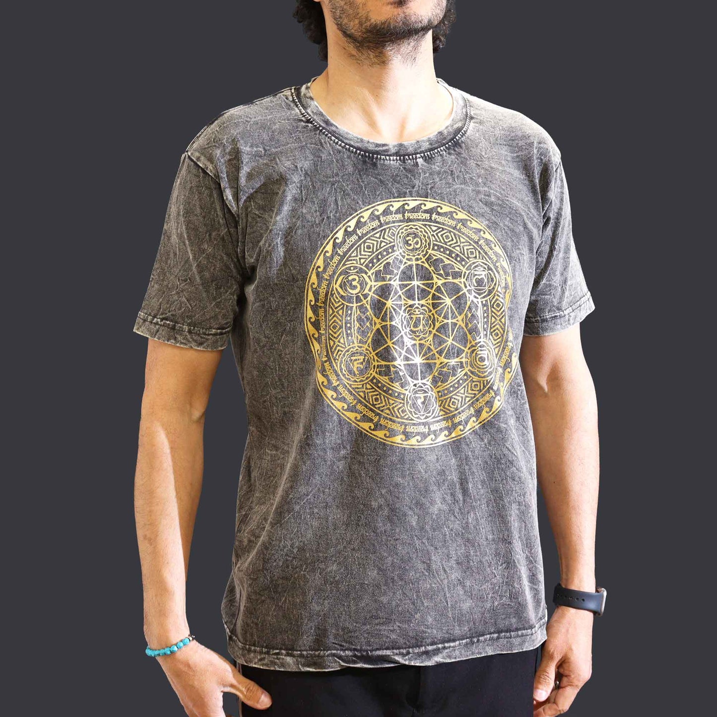 Person wearing a watch&  gray short sleeved t-shirt with a gold geometric Chakra  design on a dark background