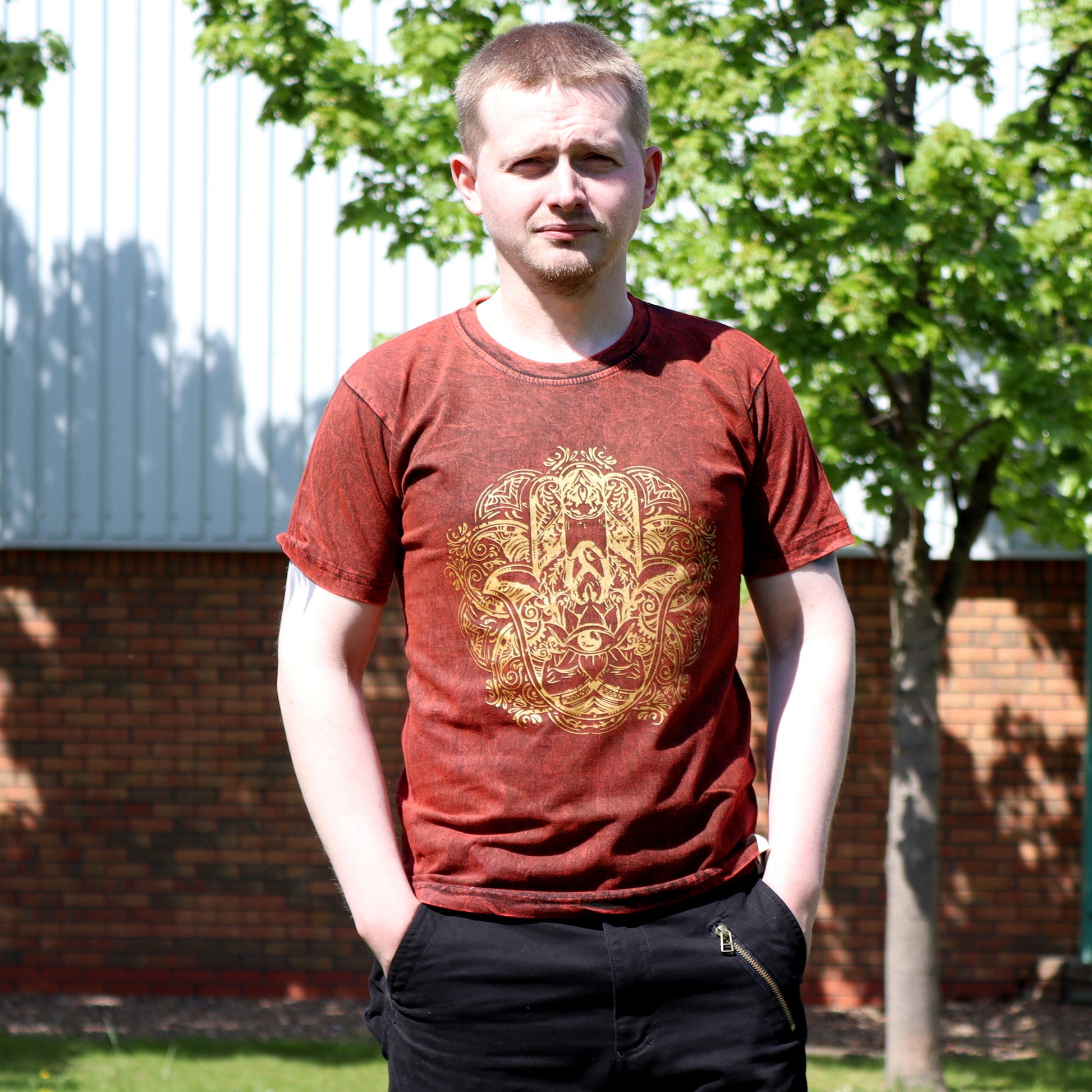Man wearing a red t-shirt with a gold hamsa design outdoors