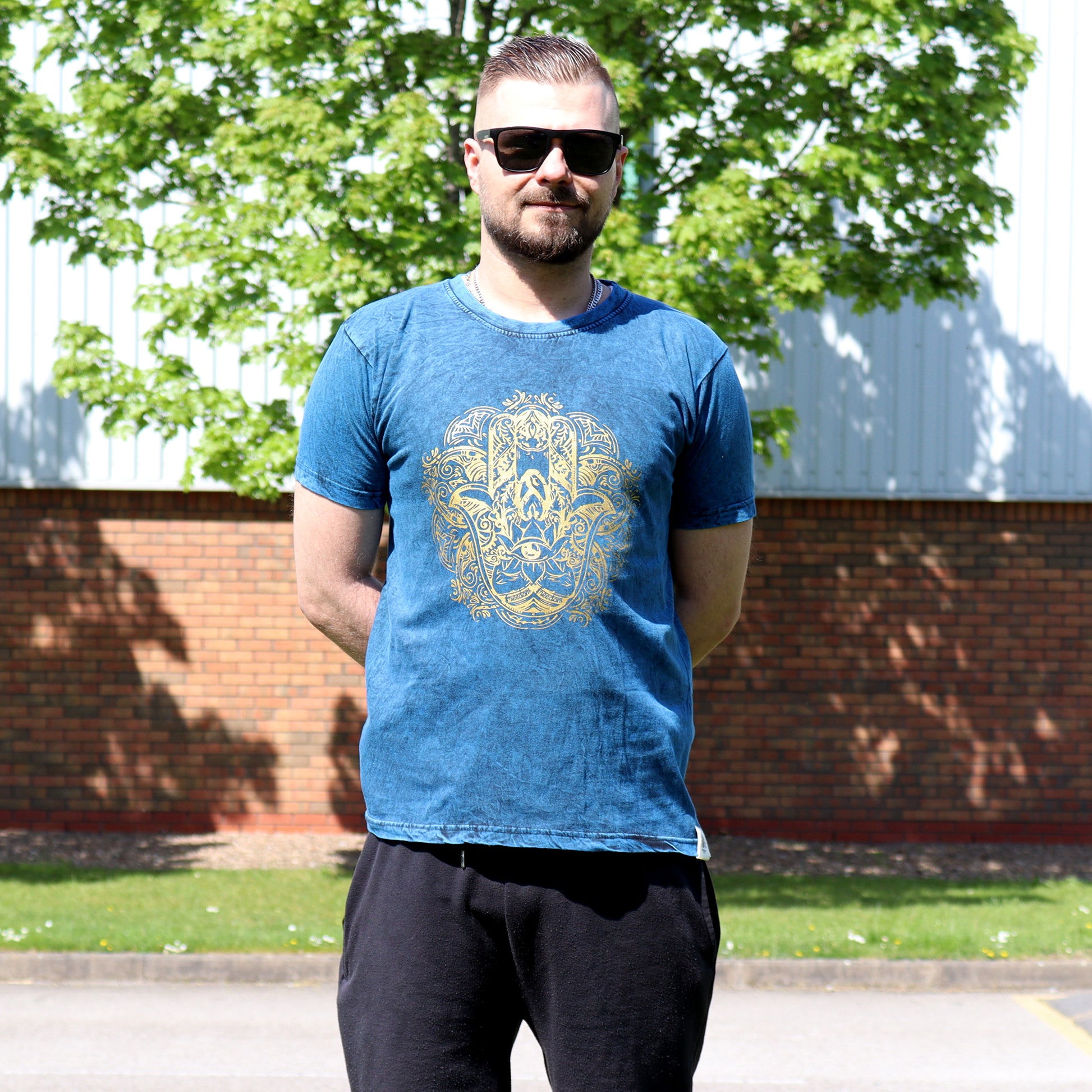 Man wearing a blue t-shirt with a gold Hamsa design standing outdoors