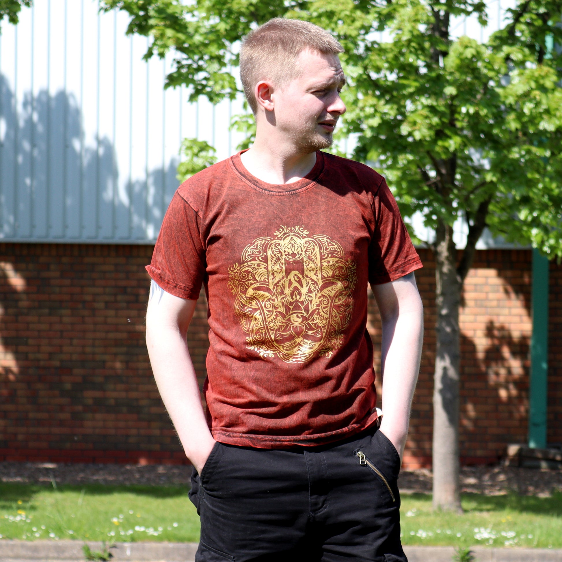 Person wearing a red t-shirt with a gold Hamsa design outdoors