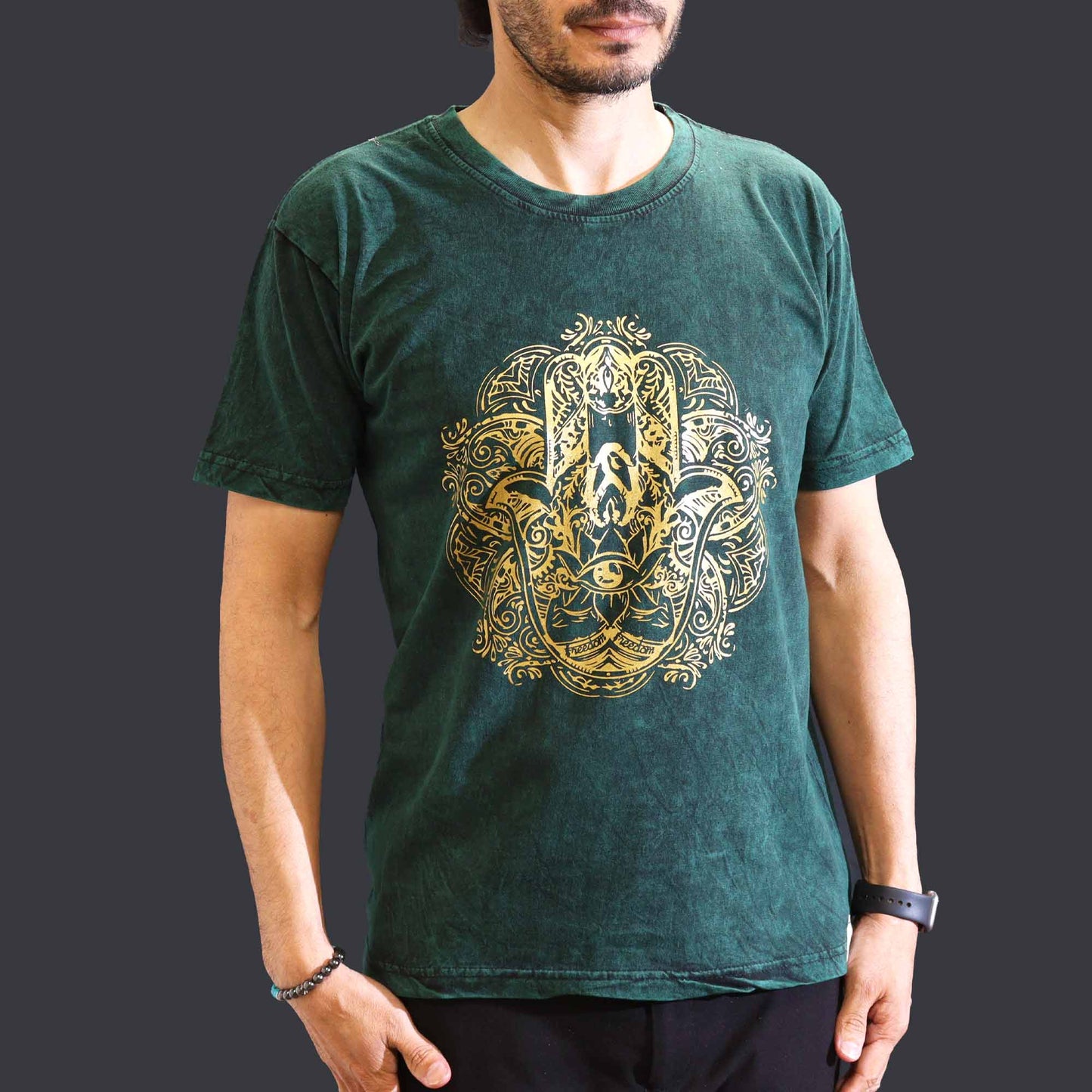 Person wearing a green t-shirt with a gold intricate hamsa design on a dark background