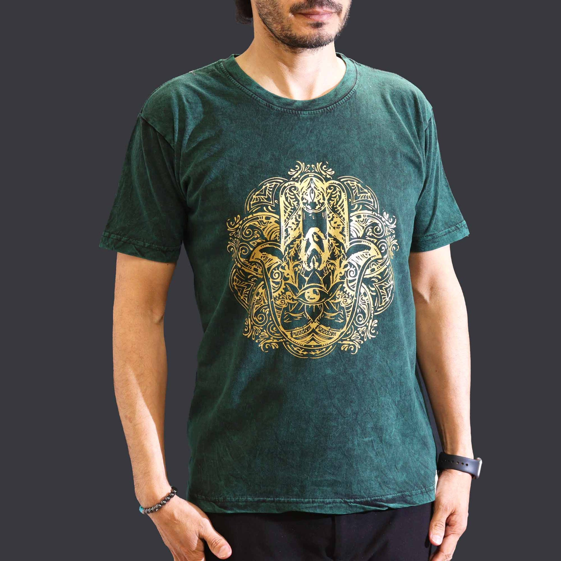 Person wearing a green t-shirt with a gold intricate hamsa design on a dark background