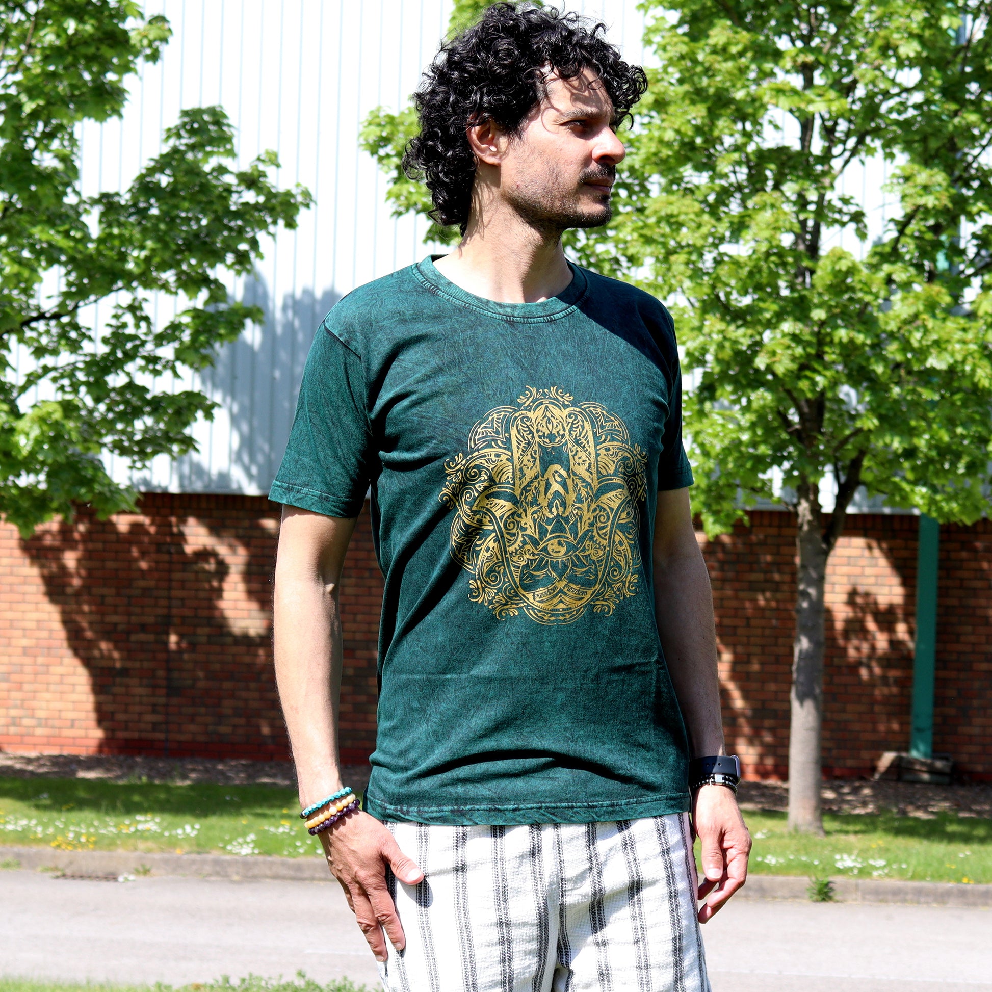 Man wearing a green t-shirt with a gold hamsa design outdoors