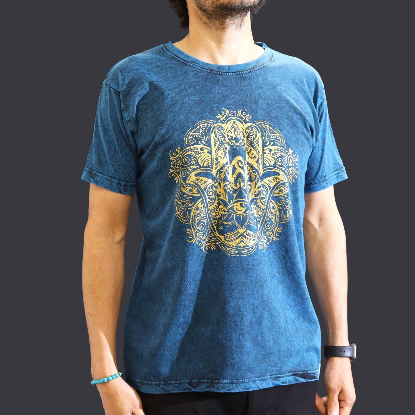 Person wearing a blue t-shirt with a yellow hamsa design on a dark background
