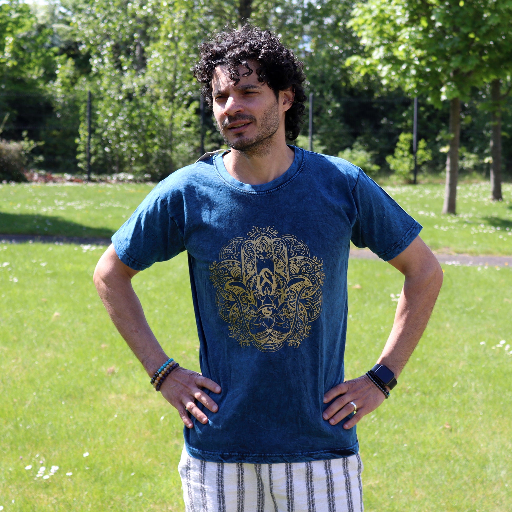 Man wearing a blue t-shirt with a gold hamsa design in a park
