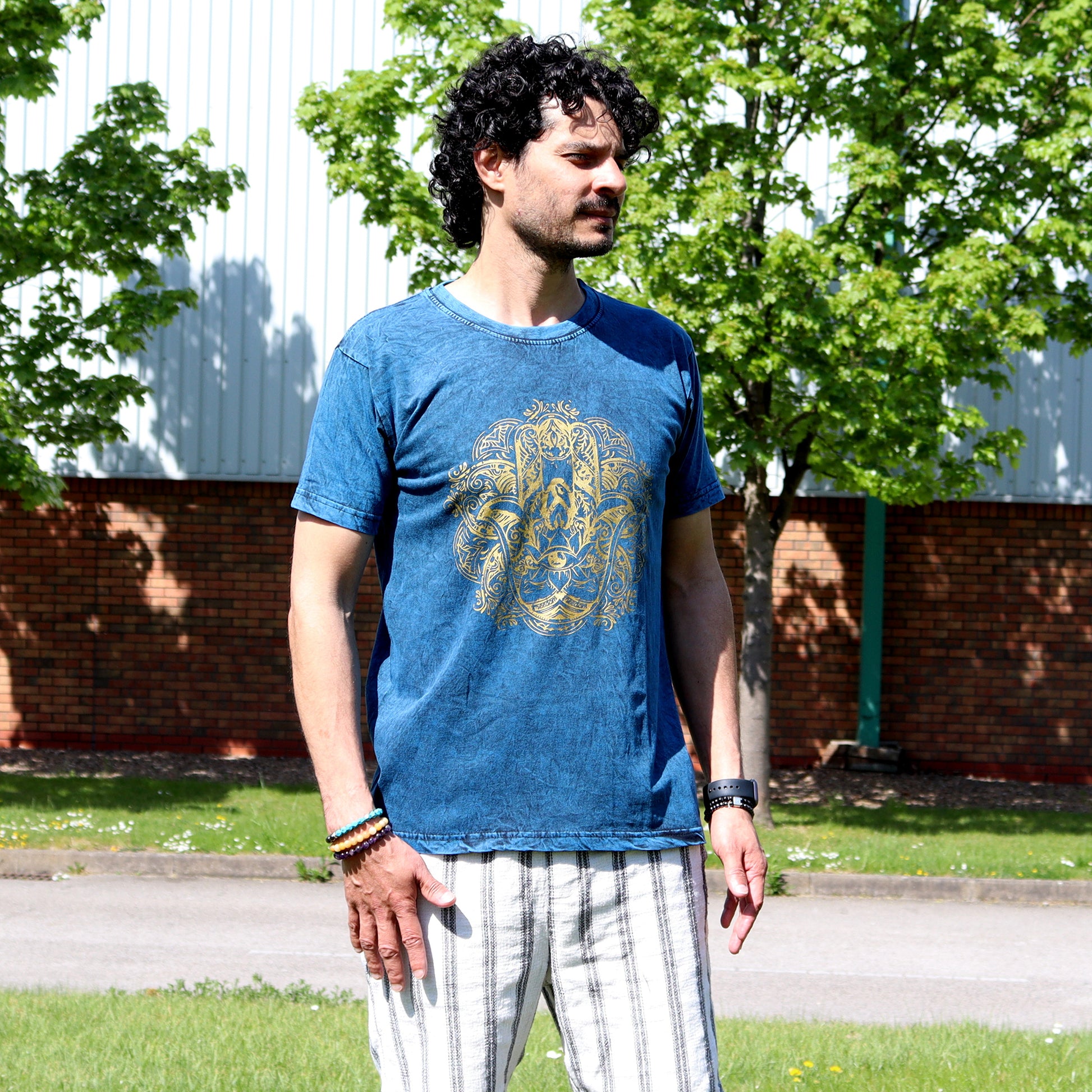 Man wearing a blue t-shirt with a gold hamsa graphic design outdoors