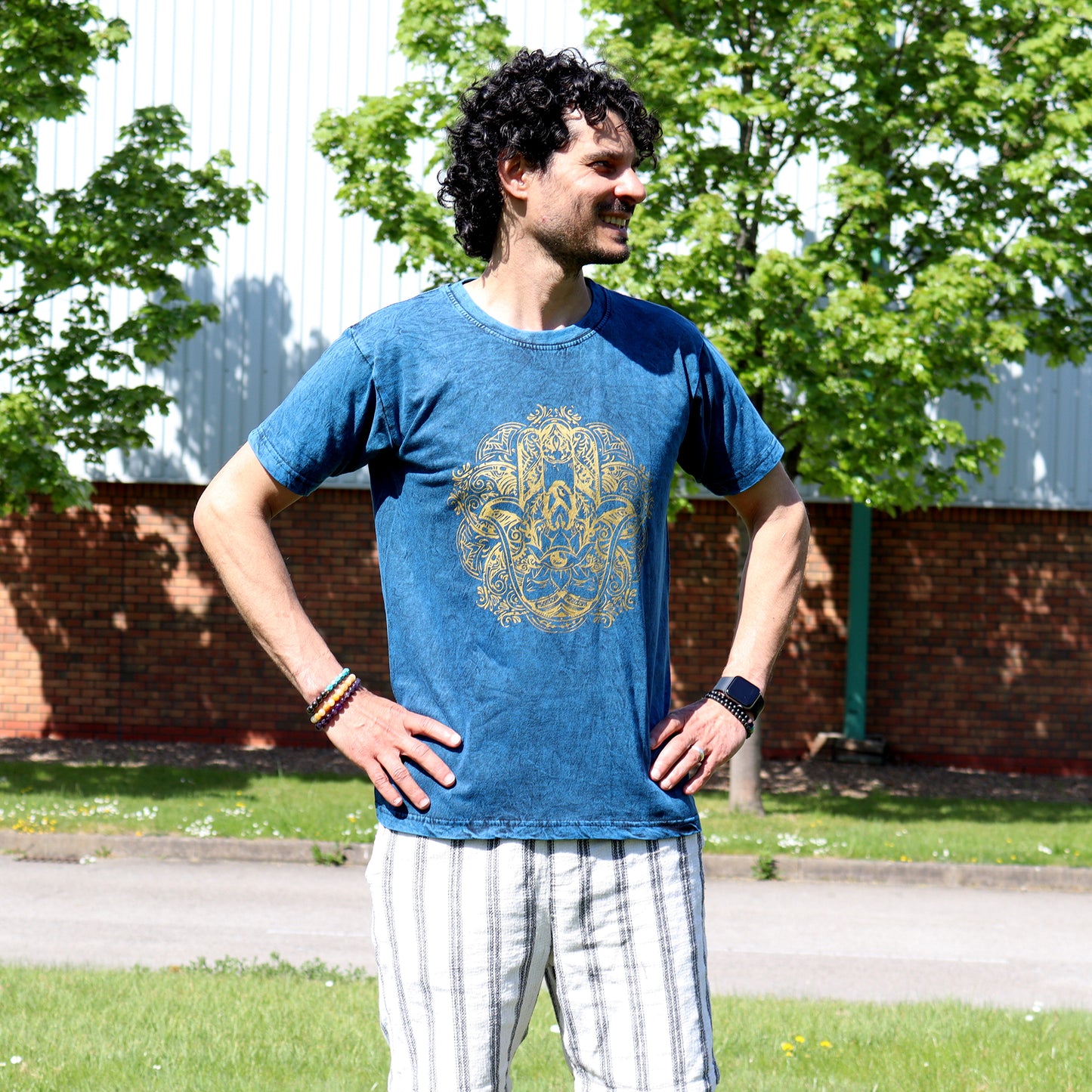 Man wearing a blue t-shirt with a gold Hamsa graphic design outdoors