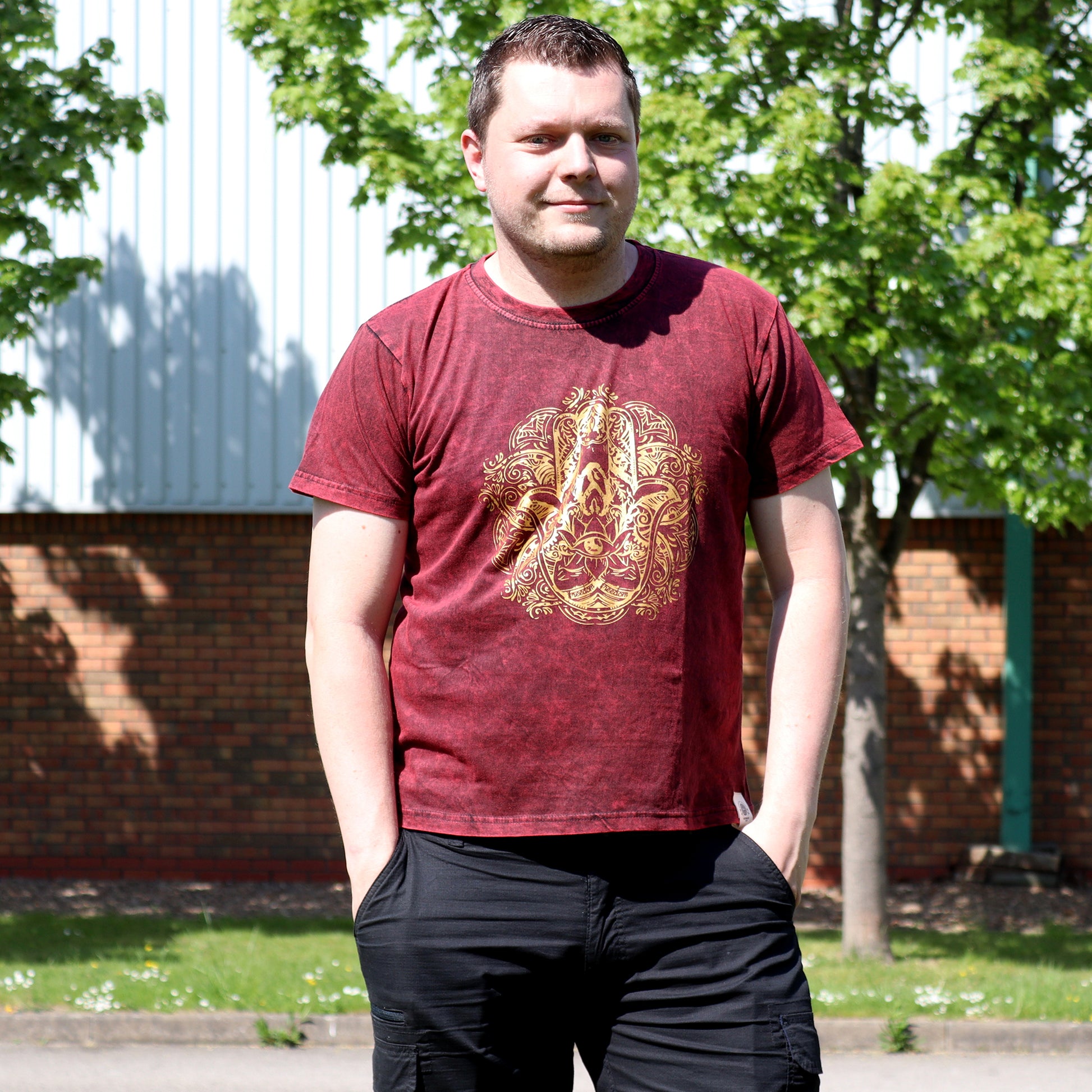 Man wearing a red t-shirt with a gold design outdoors