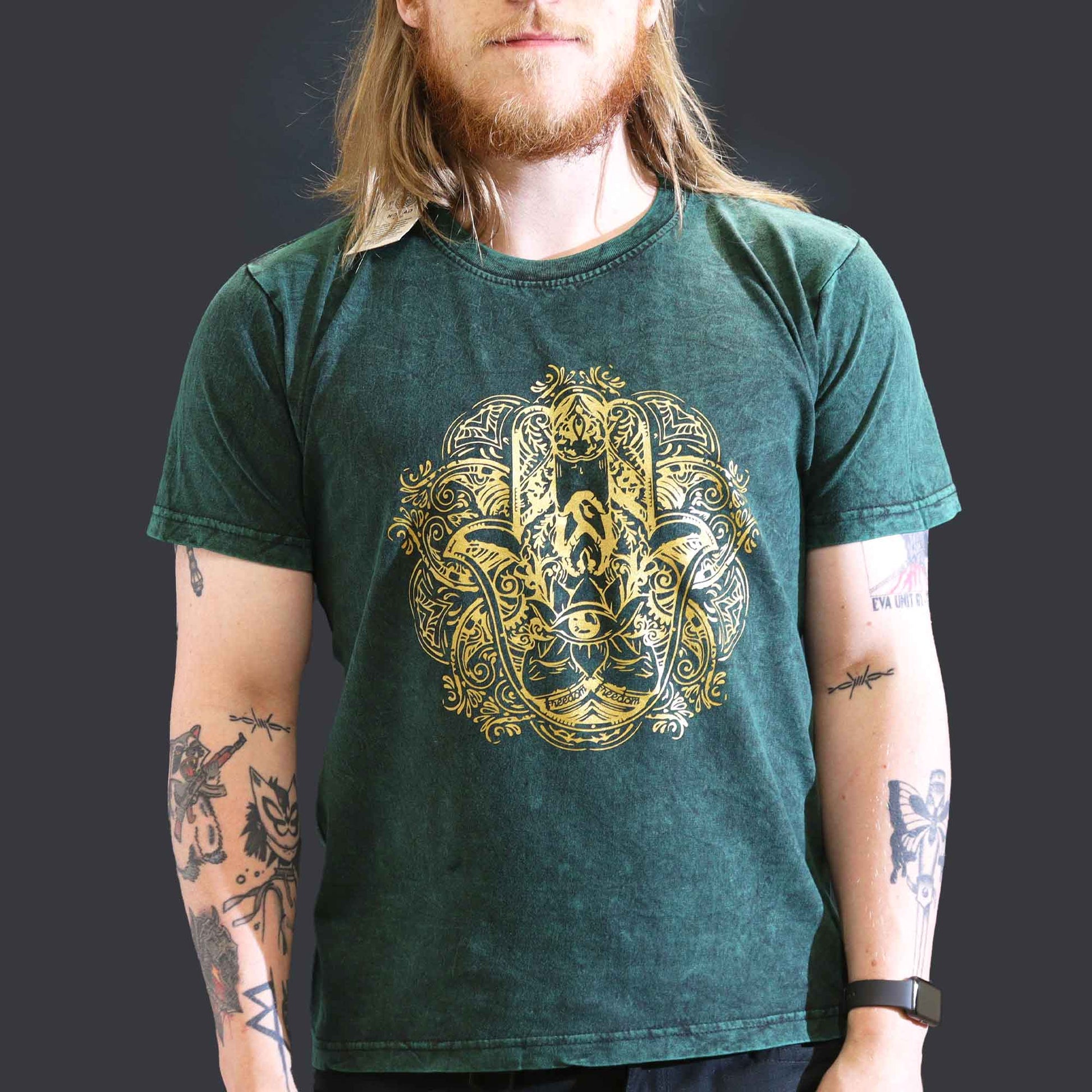 Person wearing a green t-shirt with a gold Hamsa design on a dark background