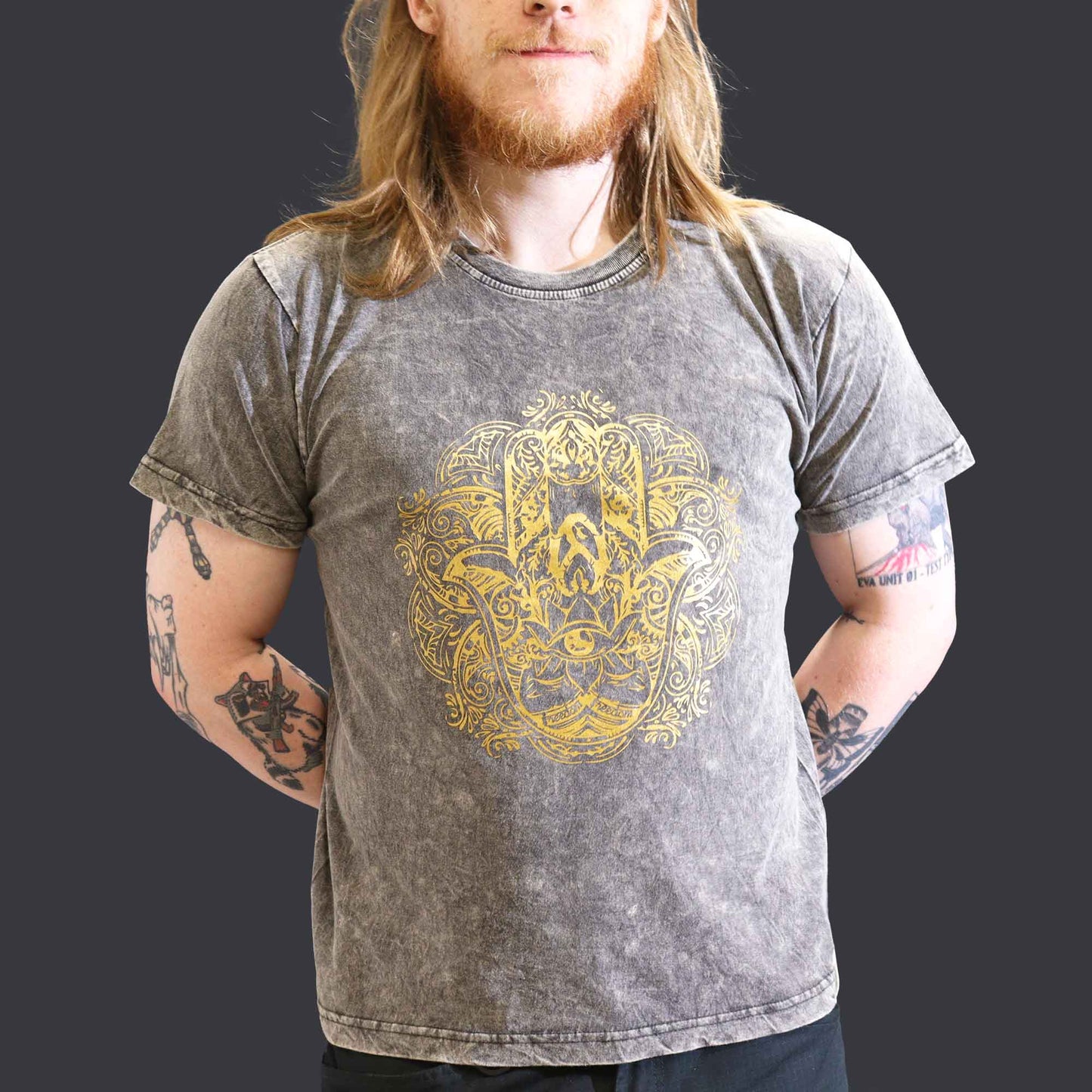 Man wearing a gray t-shirt with a gold  Hamsa graphic design on a dark background