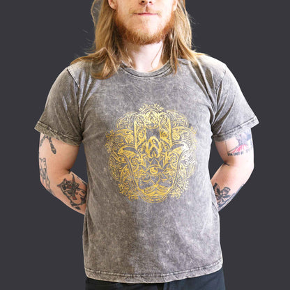 Man wearing a gray t-shirt with a gold  Hamsa graphic design on a dark background