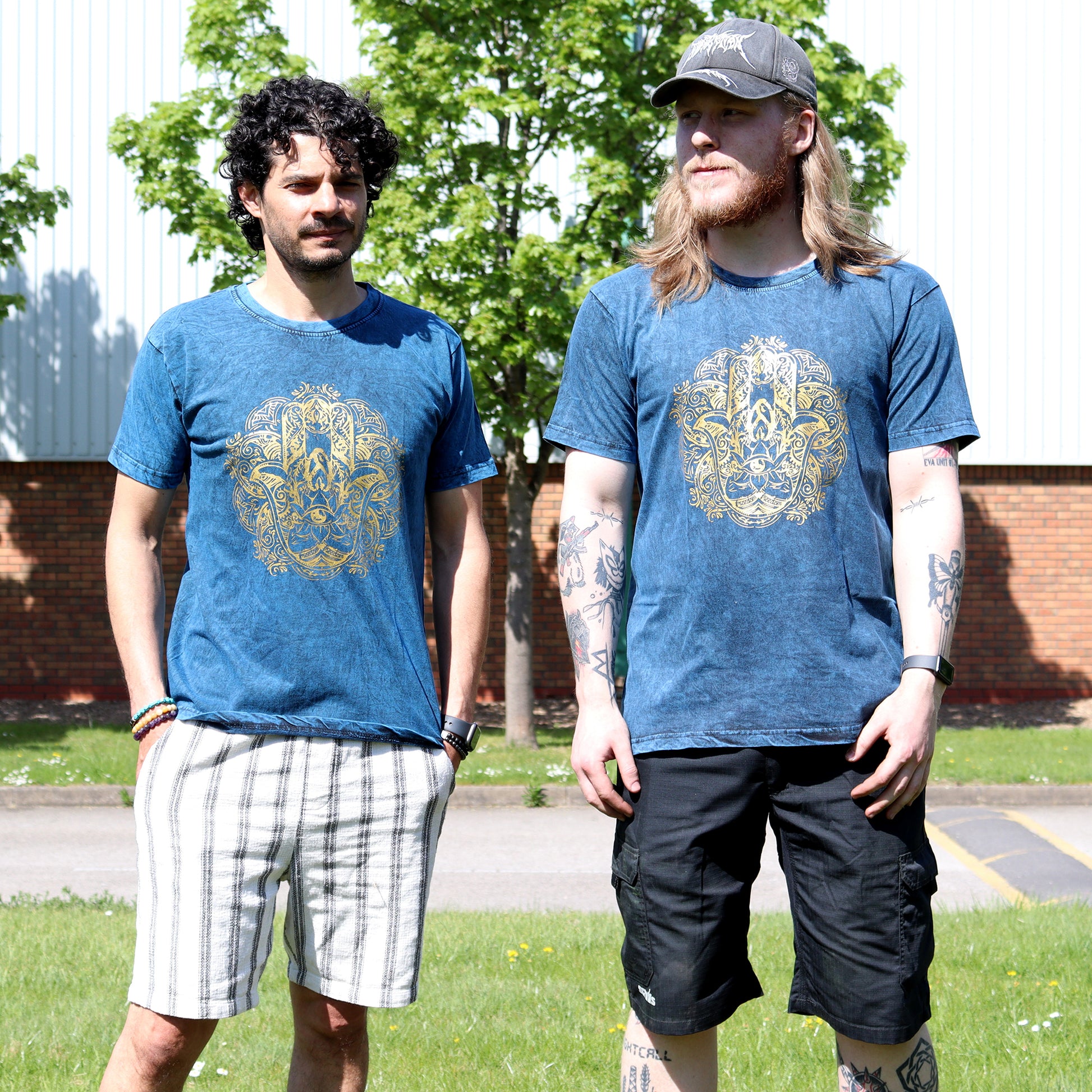 Two men wearing blue t-shirts with a gold Hamsa emblem design outdoors.