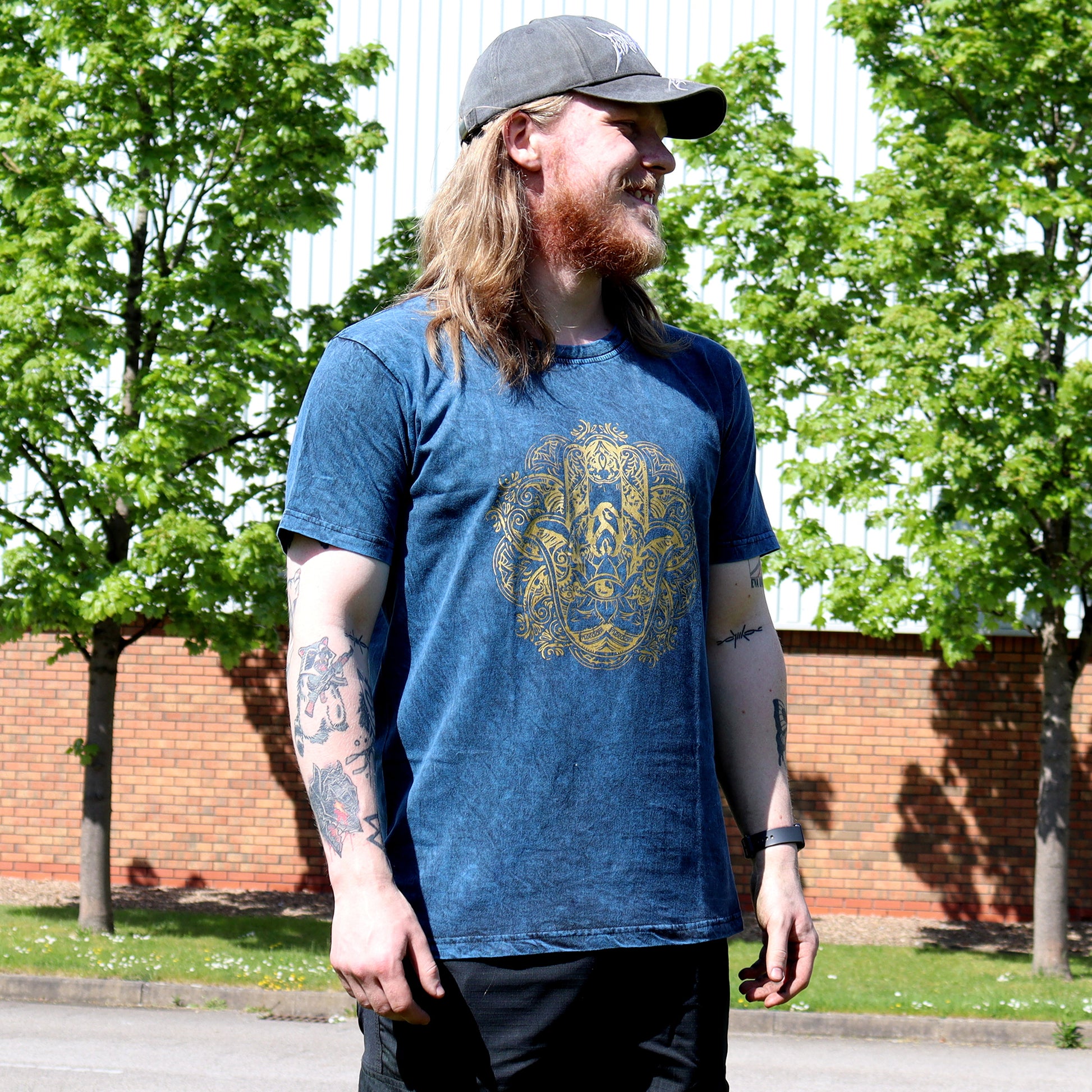 Man wearing a Grey cap & blue t-shirt with a gold Hamas design outdoors