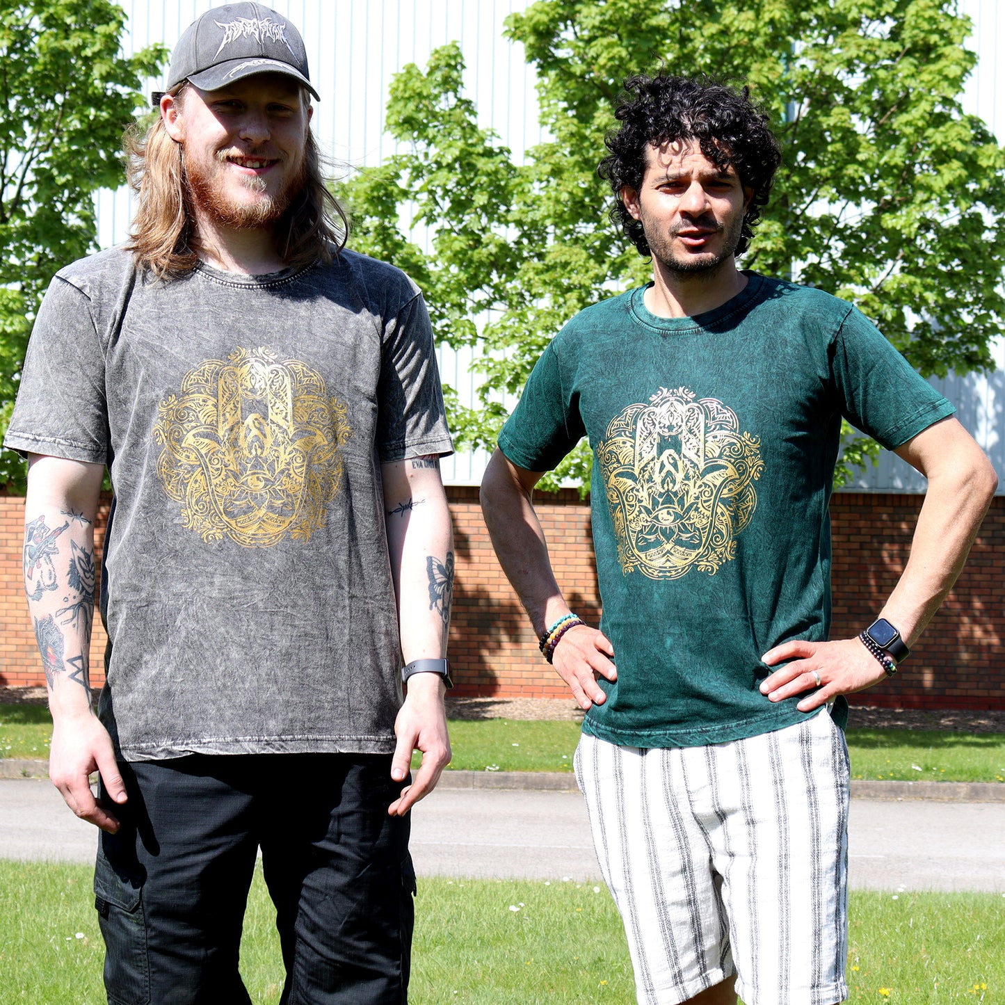 Two people wearing t-shirts with a gold Hamsa emblem design outdoors.