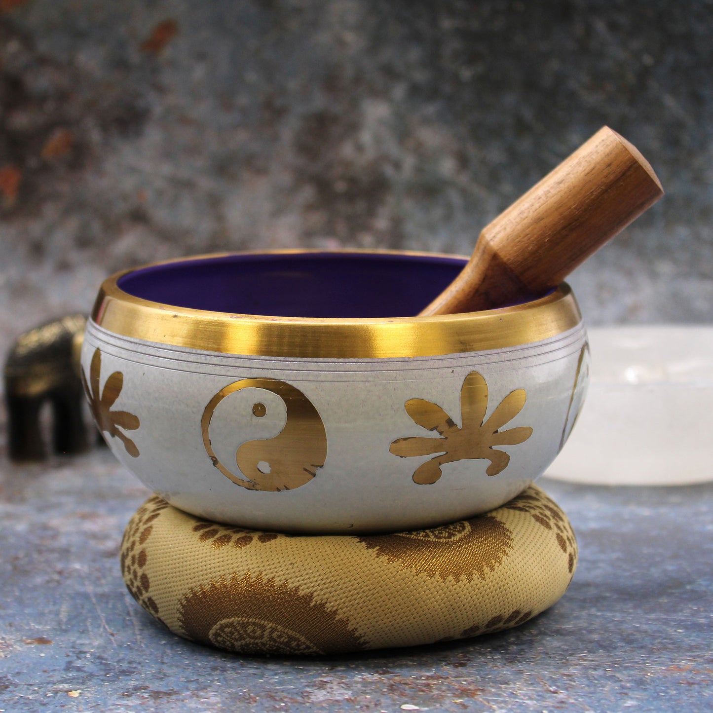 A singing bowl set including a blue and white singing bowl with a gold rim, a wooden mallet, and a black carrying bag, displayed on a white background.