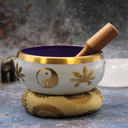 A singing bowl set including a blue and white singing bowl with a gold rim, a wooden mallet, and a black carrying bag, displayed on a white background.