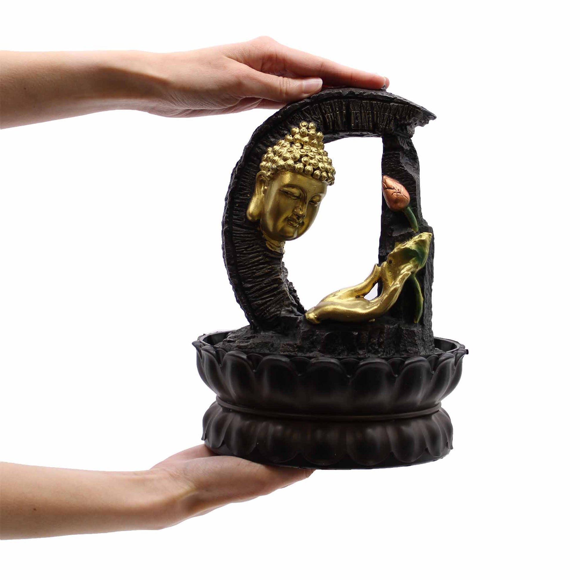 Decorative sculpture with gold Buddha figure and black base held by hands on a white background