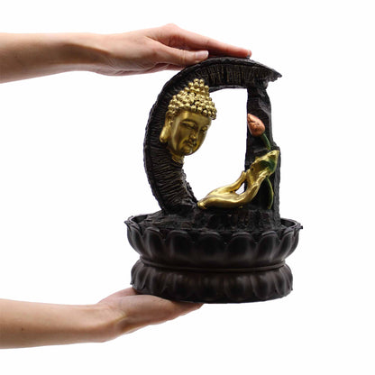Decorative sculpture with gold Buddha figure and black base held by hands on a white background