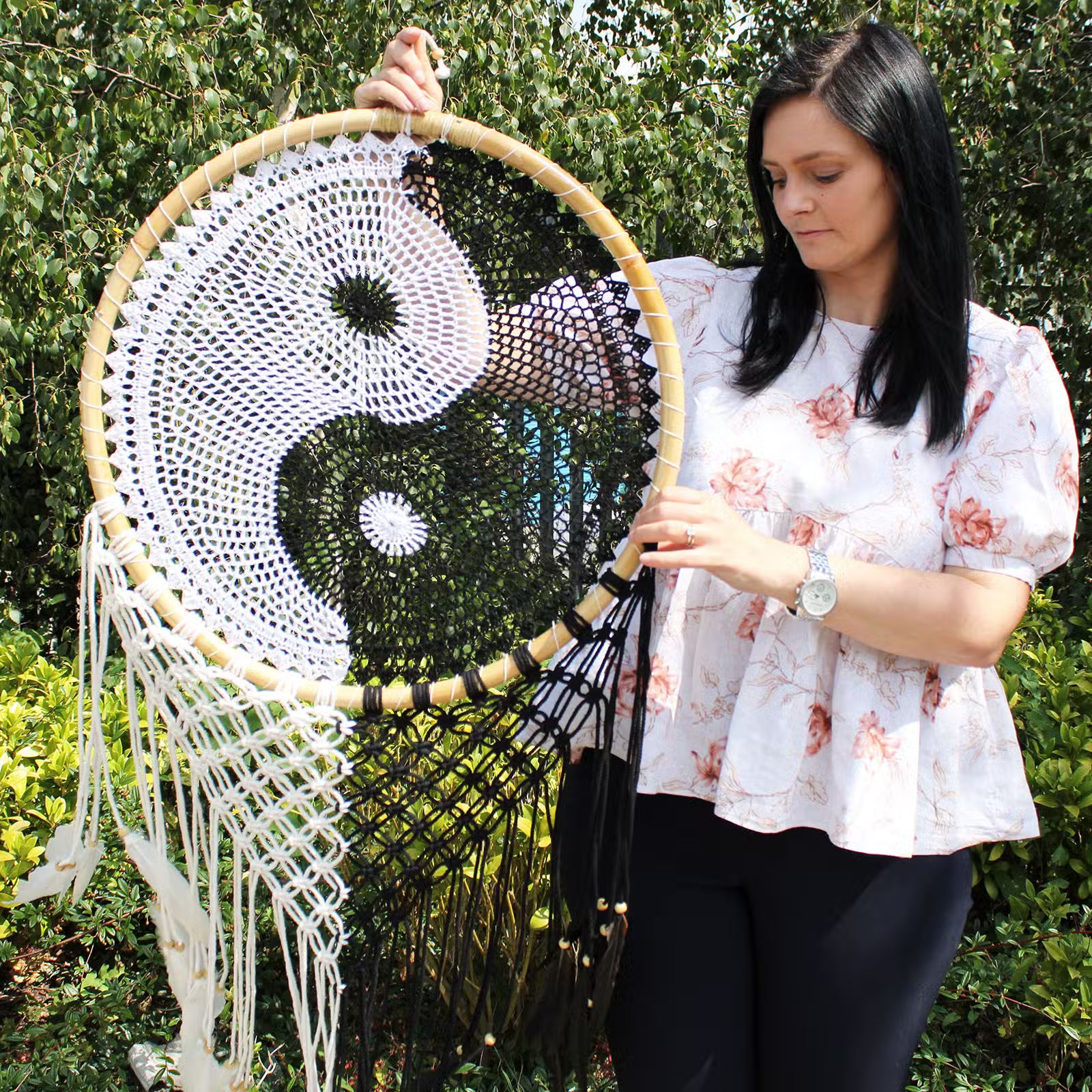 Woman holding a large decorative wall hanging Dream Catcher with a yin yang symbol outdoors.