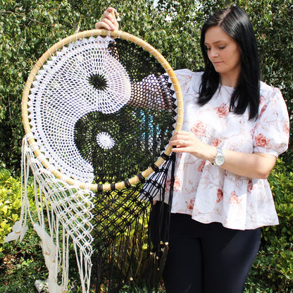 Woman holding a large decorative wall hanging Dream Catcher with a yin yang symbol outdoors.